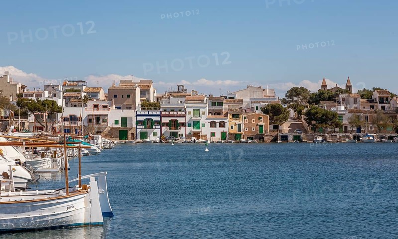 Quiet harbour with boats in the foreground and colourful buildings along the coast under a blue sky, Portocolom, Majorca, Balearic Islands, Spain, Europe