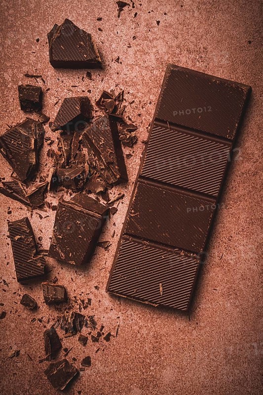 Chocolate bar, for the manufacture of confectionery, broken, crumbled, on a brown background, top view