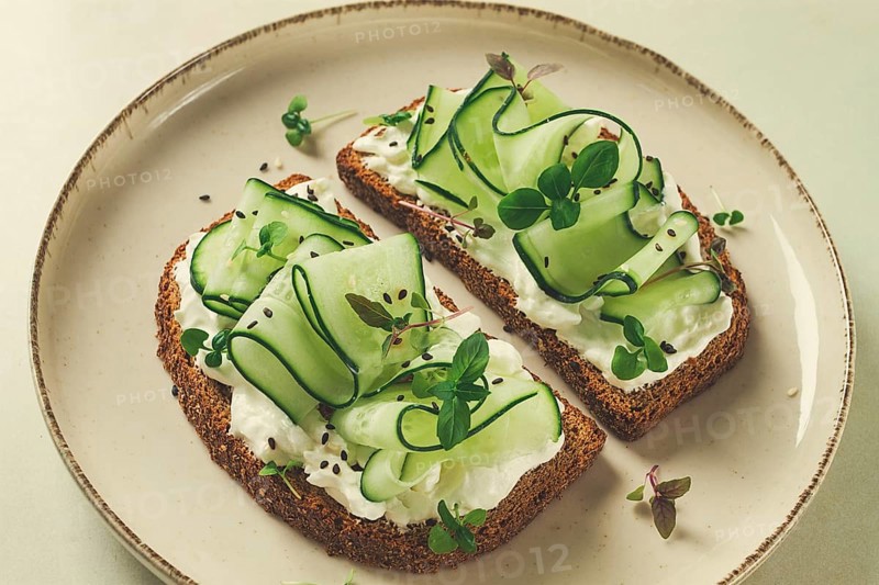 Breakfast, cereal bread sandwiches, cream cheese, sliced cucumber, with micro greenery on a light table, close-up, top view, selective focus, no people