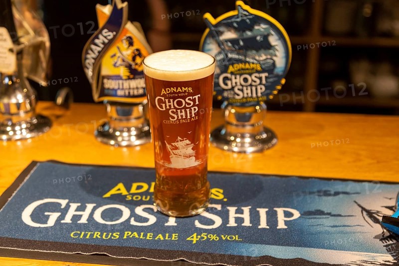 Pint glass of Adnams Ghost Ship Citrus pale Ale, on beer mat with bar pumps, Suffolk, UK