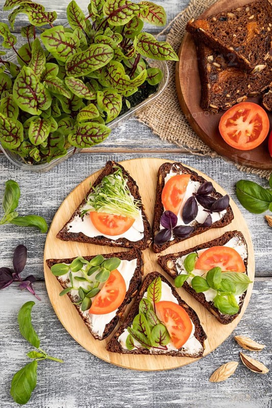 Grain rye bread sandwiches with cream cheese, tomatoes and sorrel microgreen on gray wooden background and linen textile. top view, flat lay, close up