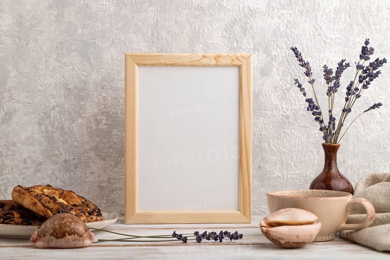White wooden frame mockup with lavender in ceramic vase, linen textile, cup of coffee and bun on gray concrete background. Blank, vertical orientation, still life
