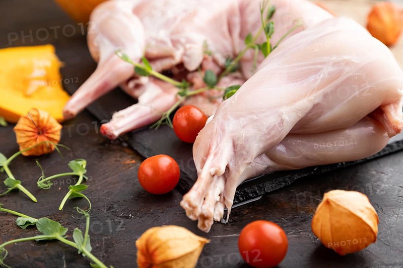 Whole raw rabbit with pumpkin, tomatoes, pea sprouts on a black concrete background and linen textile. Side view, close up, selective focus