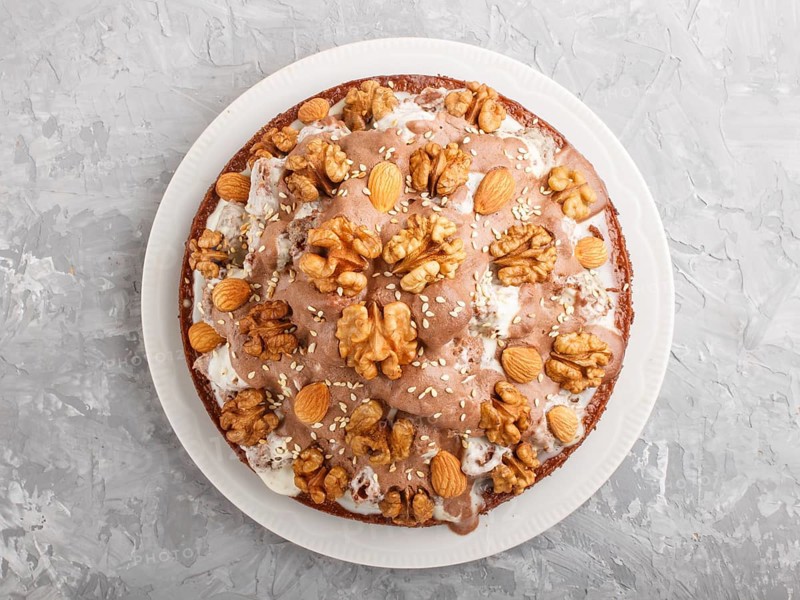 Homemade cake with milk cream, cocoa, almond, hazelnut on a gray concrete background with orange textile. Top view, flat lay, close up