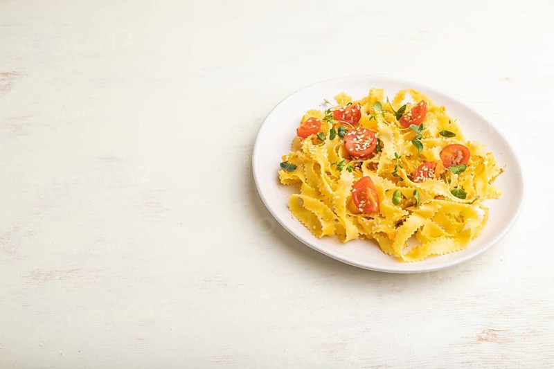 Reginelle semolina pasta with tomato, eggs, sesame and microgreen sprouts on a white wooden background. Side view, copy space