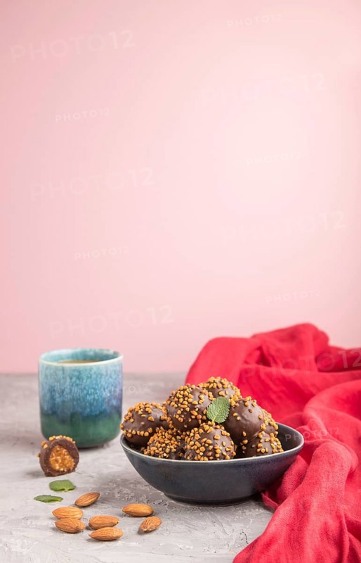 Chocolate caramel ball candies with almonds and a cup of coffee on a gray and pink background and red textile. Side view, copy space, selective focus