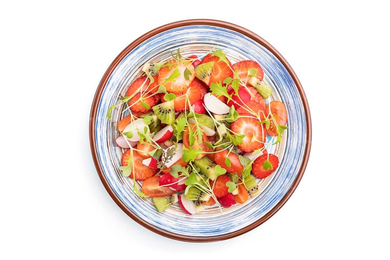 Vegetarian fruits and vegetables salad of strawberry, kiwi, tomatoes, microgreen sprouts isolated on white background. Top view, flat lay, close up