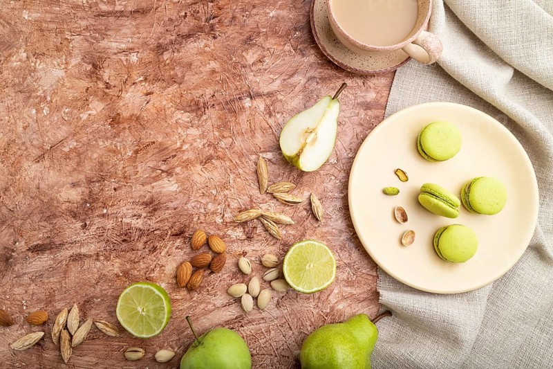 Green macarons or macaroons cakes with cup of coffee on a brown concrete background and linen textile. Top view, flat lay, copy space