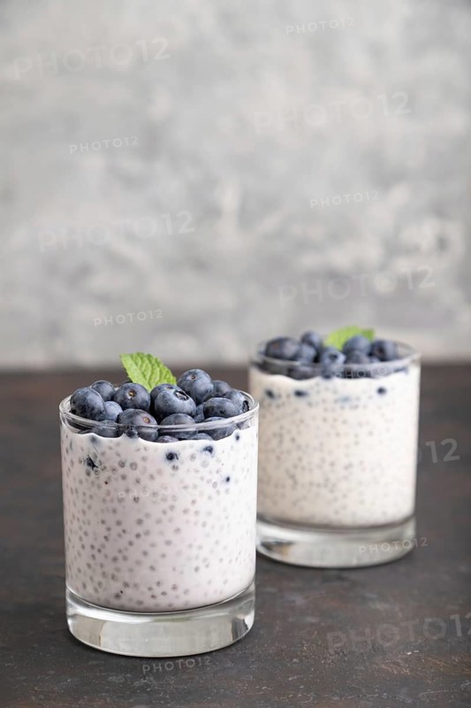 Yogurt with blueberry and chia in glass on black concrete background. Side view, close up, copy space