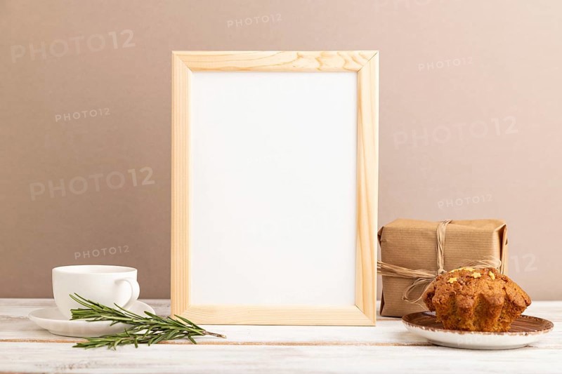 White wooden frame mockup with cup of coffee and cake on brown background. Blank, side view, still life