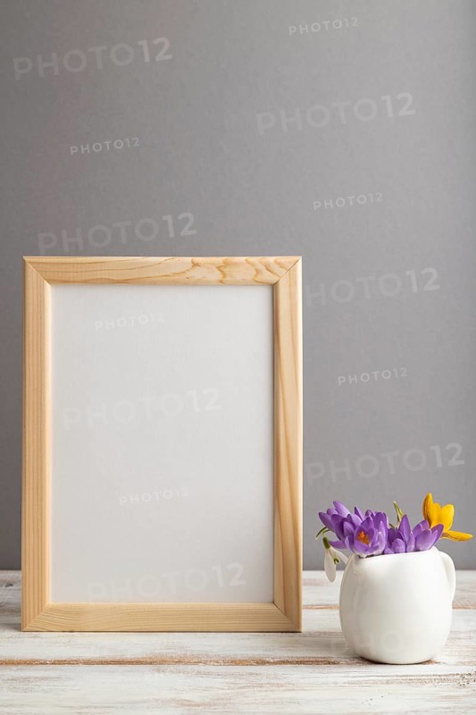 Beige wooden frame mockup with snowdrop crocus flowers on gray paper background. Blank, vertical orientation, still life, copy space
