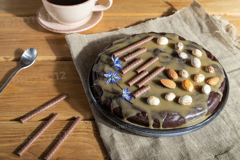Homemade chocolate brownie cake with caramel cream and almonds with cup of coffee on wooden background and linen textile. Side view, hard light, close up