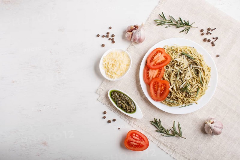 Spaghetti pasta with pesto sauce, tomatoes and cheese on a linen tablecloth on white wooden background. top view, copy space