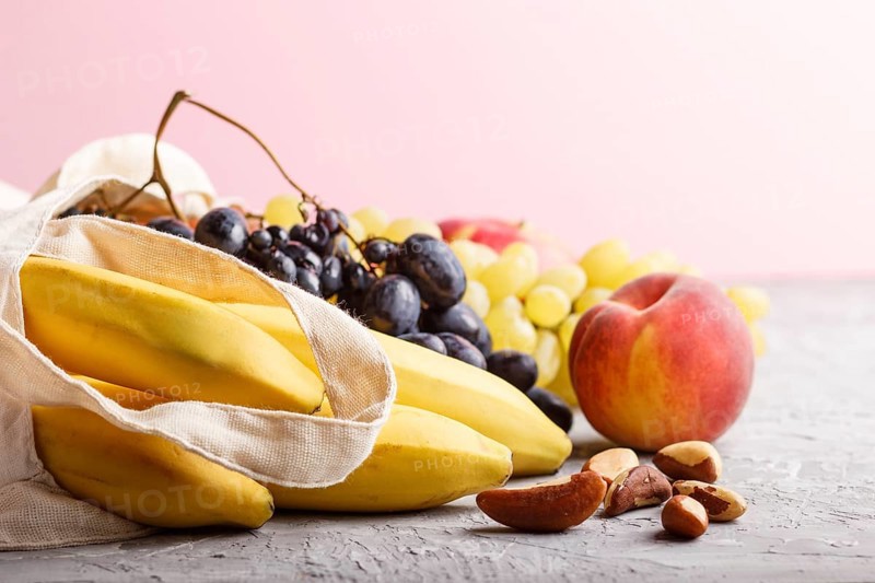 Fruits in reusable cotton textile white bag. Zero waste shopping, storage and recycling concept, eco friendly lifestyle. Side view, close up, copy space. Peach, apple, banana, grape