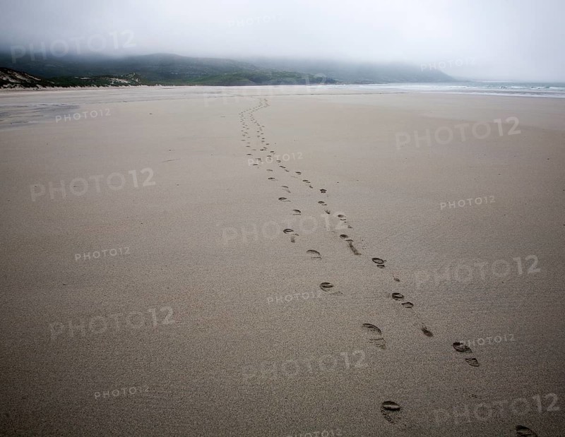 Foot step prints in wet sand on a cloudy overcast day at Traigh Eais beach, Barra, Outer Hebrides, Scotland, UK