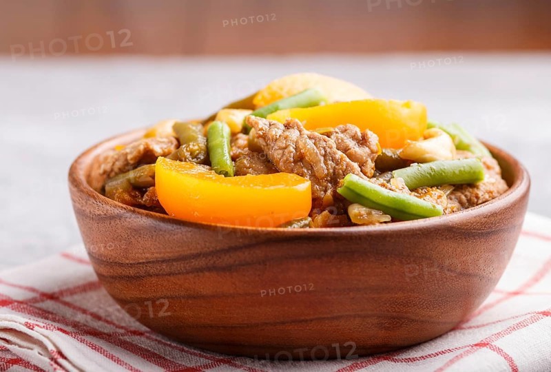 Fried pork with peaches, cashew and green beans in a wooden bowl on a gray concrete background. Side view, close up, chinese cuisine