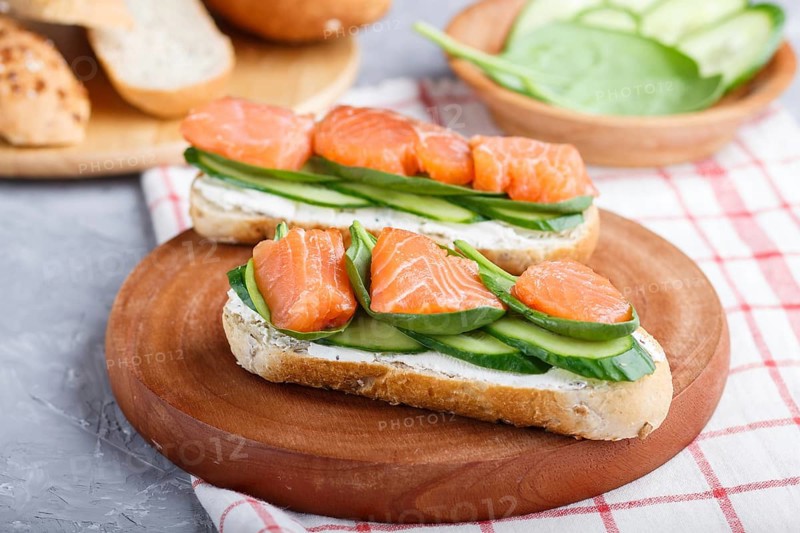 Smoked salmon sandwiches with cucumber and spinach on wooden board on a linen background. side view, close up