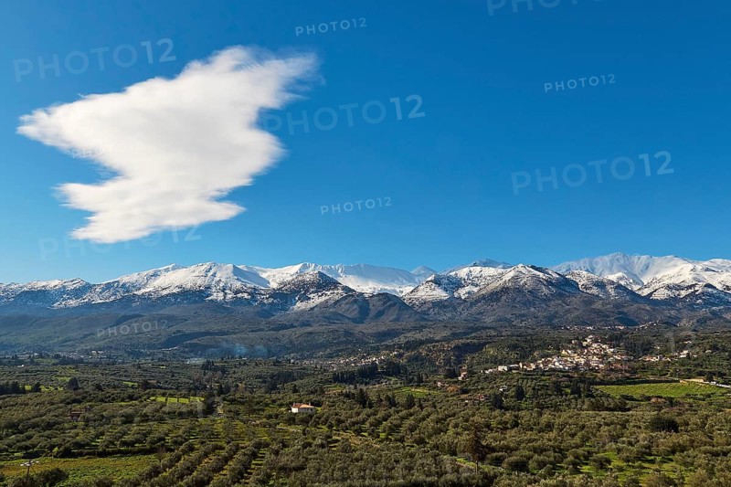 Snow-capped mountains under blue sky and clouds with green valley and village in the foreground, Green olive groves, Lefka Ori, White Mountains, Mountain massif, West, Crete, Greece, Europe