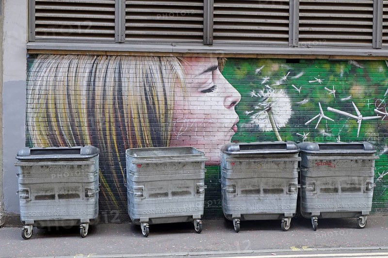A mural shows a girl blowing a dandelion in front of rubbish containers, Mural Trail, Glasgow, Scotland, Great Britain