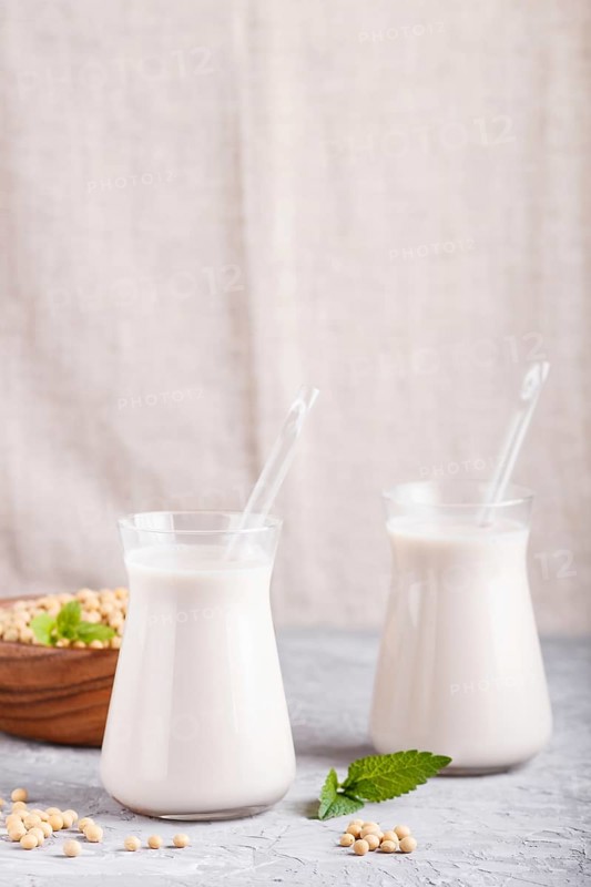 Organic non dairy soy milk in glass and wooden plate with soybeans on a gray concrete background. Vegan healthy food concept, close up, side view, copy space