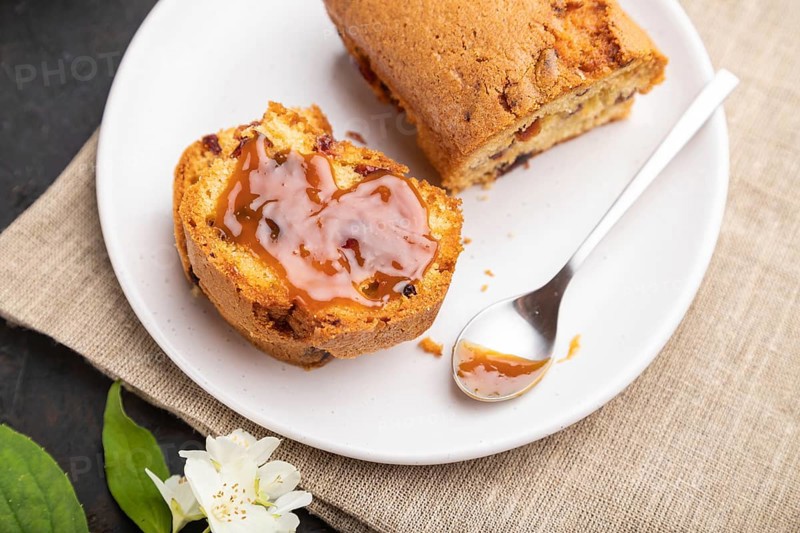 Homemade cake with raisins, almonds, soft caramel and a cup of coffee on a black concrete background and linen textile. Side view, close up, selective focus