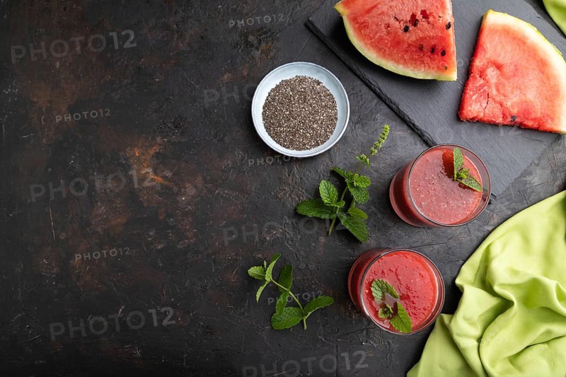 Watermelon juice with chia seeds and mint in glass on a black concrete background with green textile. Healthy drink concept. Top view, copy space, flat lay