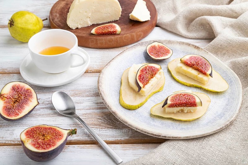 Summer appetizer with pear, cottage cheese, figs and honey on a white wooden background and linen textile. Side view, close up