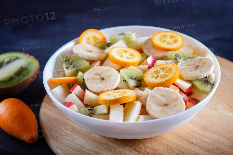 Vegetarian salad of bananas, apples, pears, kumquats and kiwi on black woodem background, close up, selective focus