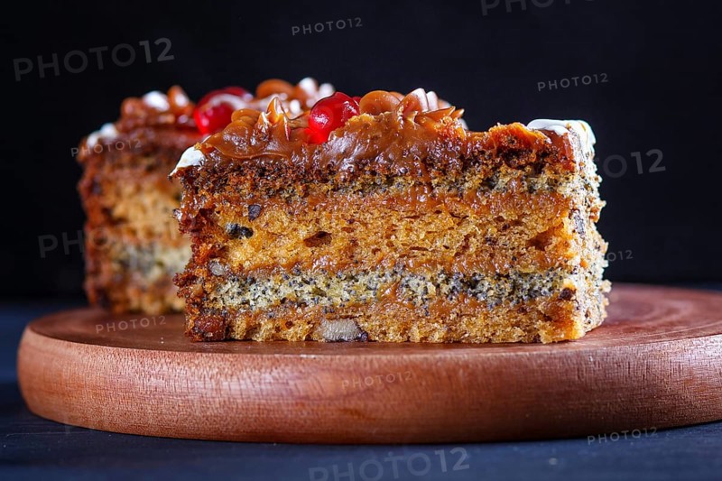 A piece of cake with caramel cream and poppy seeds on a wooden kitchen board. close up, selective focus, black background