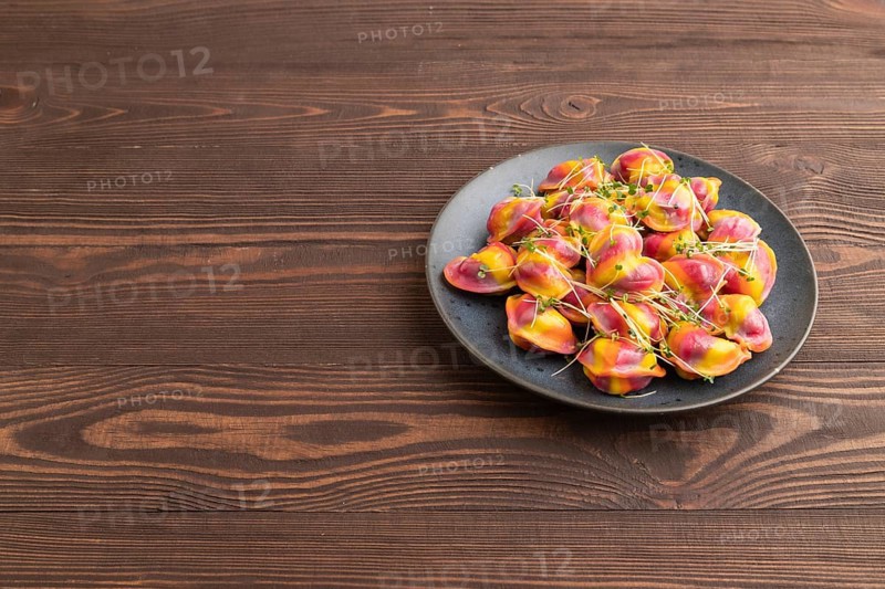 Rainbow colored dumplings with pepper, herbs, microgreen on brown wooden background. Side view, copy space