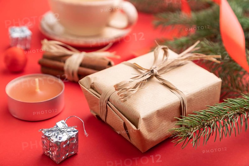 Christmas or New Year composition. Decorations, box, cinnamon, fir and spruce branches, cup of coffee, on a red paper background. Side view, cclose up, selective focus