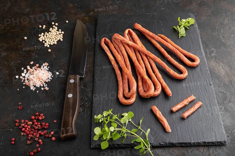 Traditional polish smoked pork sausage kabanos on a slate cutting board with salt and pepper on black concrete background. Side view, close up