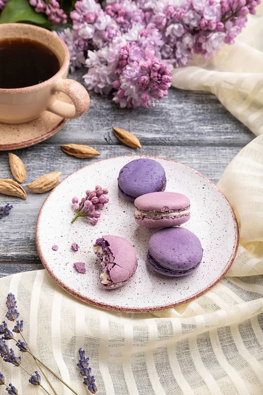 Purple macarons or macaroons cakes with cup of coffee on a gray wooden background and white linen textile. Side view, close up