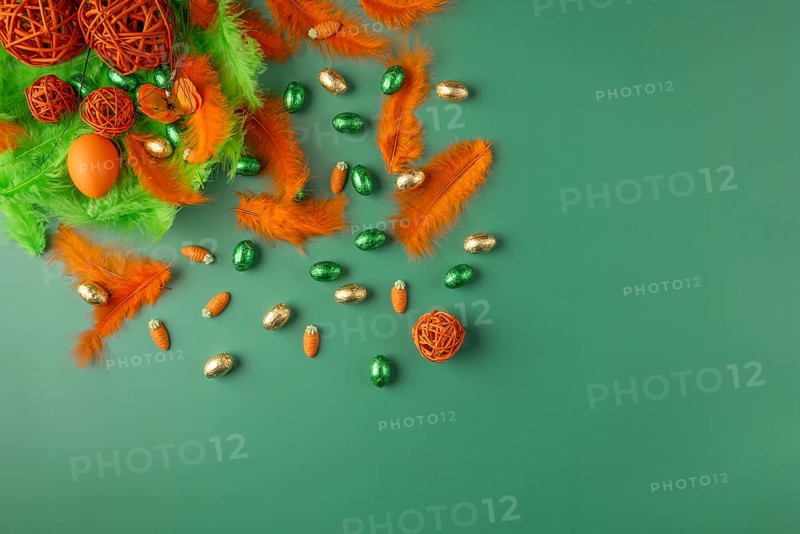 Spring-like Easter arrangement with feathers and chocolate eggs in green and orange on a green background