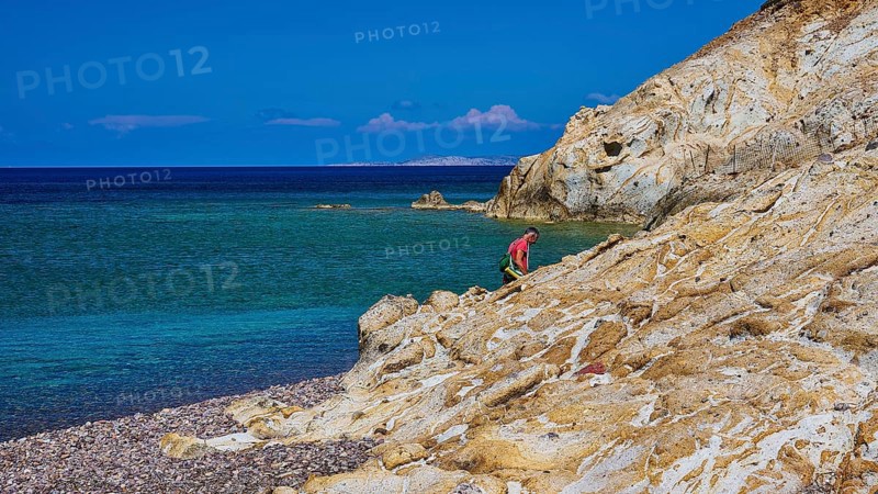 A man climbing on rocks on a coast with clear sky and clear water, Lambi beach, pebble beach, Patmos, Dodecanese, Greek Islands, Greece, Europe