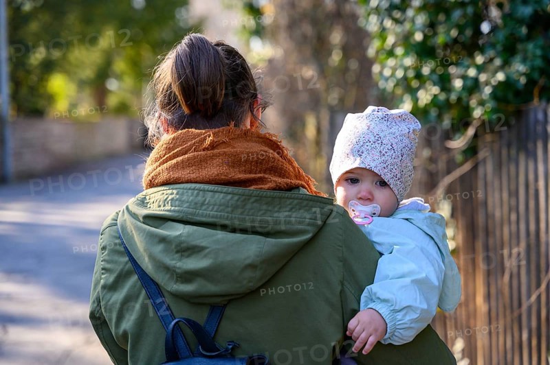 Mother holding her child with a cold and a dummy in her mouth on the way to the paediatrician