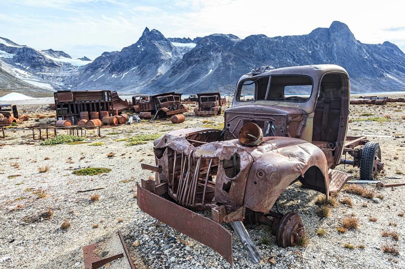 Rusted car and oil drums in front of steep mountains, remains of a US airbase from the Second World War, Ikateq Fjord, East Greenland, Greenland, North America