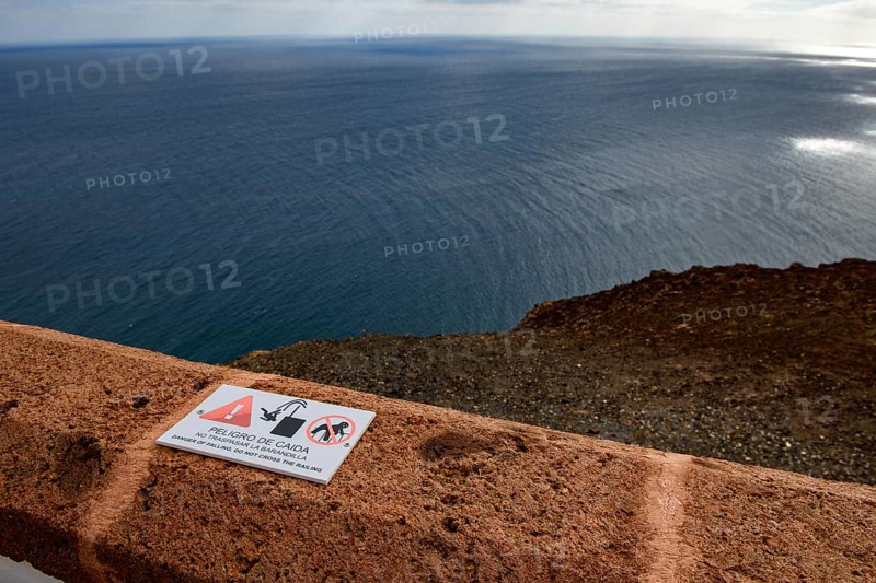 View from building complex of lighthouse Faro de la Entallada from 50s year 1953 1954 on 183 metres high rocks of cliff east coast of Fuerteventura on Atlantic Ocean, in the foreground on wall cornice warning sign warning of danger of falling into the depth, Las Playitas, Tuineje, Las Palmas, Fuerteventura, Canary Islands, Spain, Europe