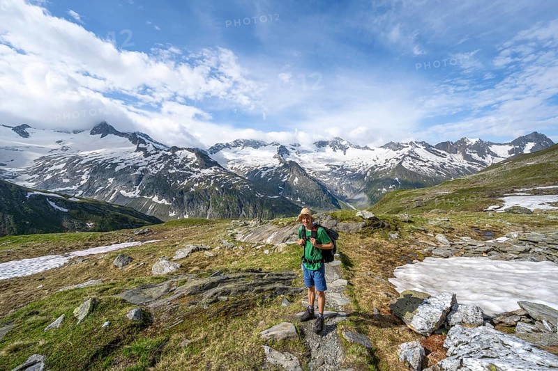 Mountaineer on hiking trail in picturesque mountain landscape, mountain peak with snow and glacier Schwarzensteinkees, Hornkees and Waxeggkees, summit Schwarzenstein, Hornspitzen and Großer Möseler, Berliner Höhenweg, Zillertal Alps, Tyrol, Austria, Europe