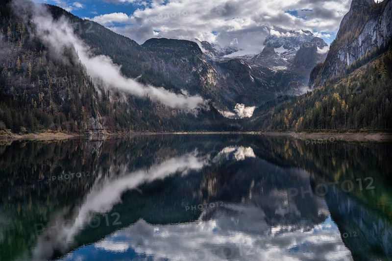 The Vordere Gosausee in autumn. In the background, the Dachstein mountain range in clouds. Partly blue sky and sun. Cloudy forest. Vorderer Gosausee, Gosau, Gosau Valley, Salzkammergut, Upper Austria, Austria, Europe