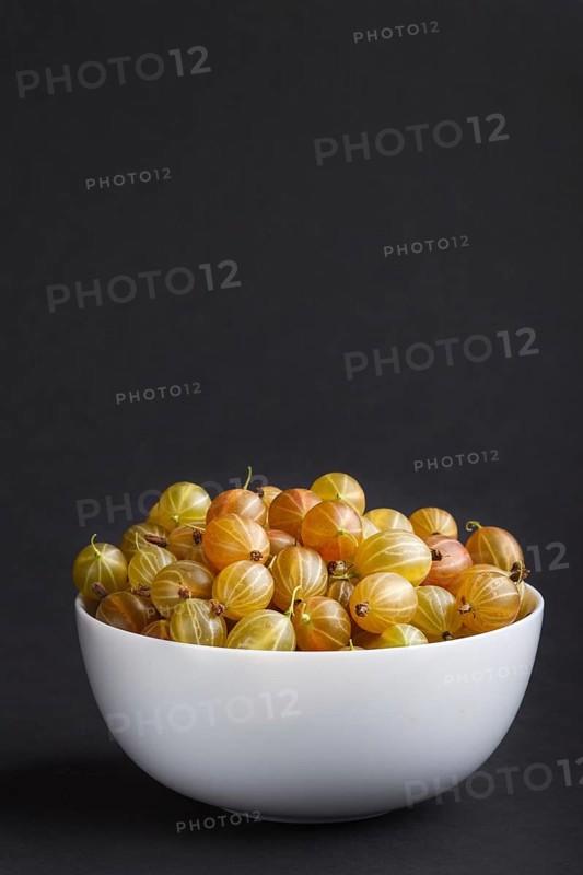 Fresh green gooseberry in white bowl on black background. side view, copy space, close up