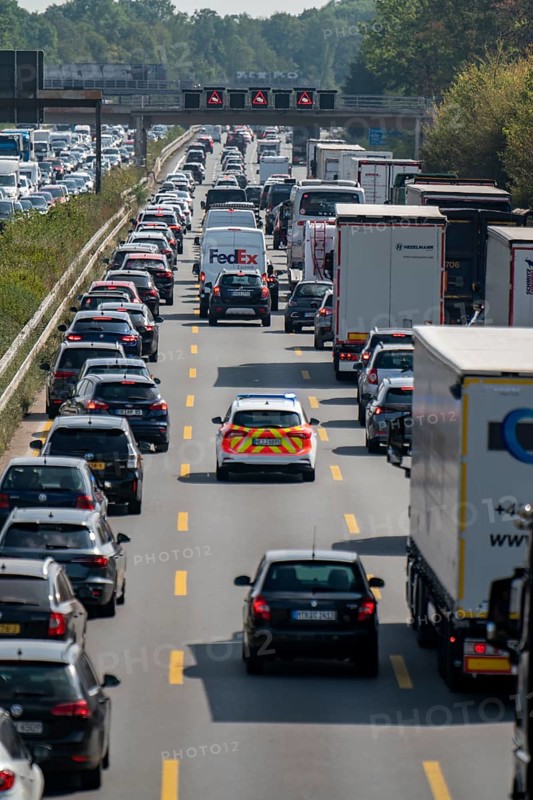 Emergency ambulance with flashing blue lights and siren working its way through a traffic jam on the A3 motorway, over 8 lanes, in both directions, in front of the Leverkusen motorway junction looking north, Friday afternoon heavy traffic, delays due to the traffic jam, Leverkusen, North Rhine-Westphalia, Germany, Europe