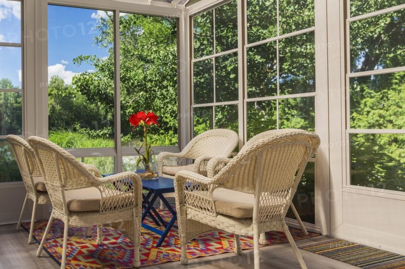 Beige wicker armchairs and blue wooden table in sunroom at back of luxurious residential home, Quebec, Canada, North America
