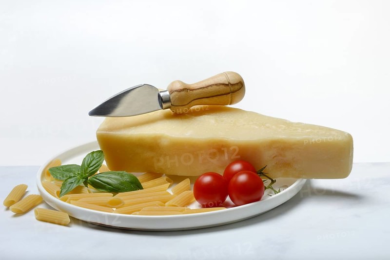 A piece of Parmesan cheese with cheese knife, pasta and tomatoes, Italy, Europe