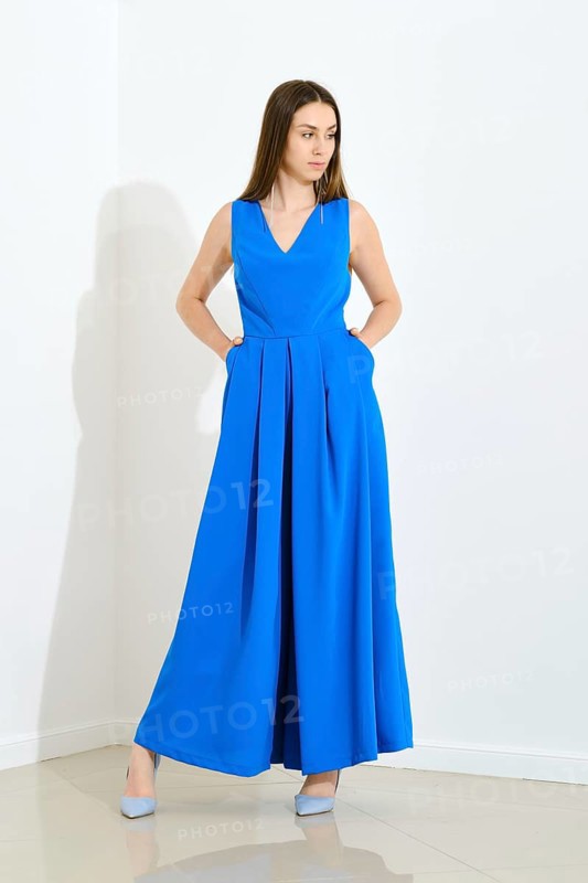 Full length portrait of stylish trendy woman in blue long sleeveless dress holding her hands in pockets