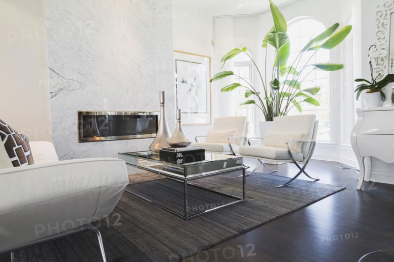 Living room with white leather and chrome sofa, armchairs, glass-top coffee table, gas fireplace with grey nuanced marble mantle-piece inside a luxurious residential home, Quebec, Canada, North America