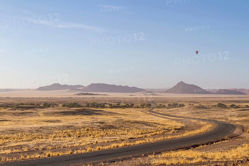Landscape in arid environment with a road, mountains in the background and a hot air balloon in the sky, Sossusvlei landscape, Namibia, Africa