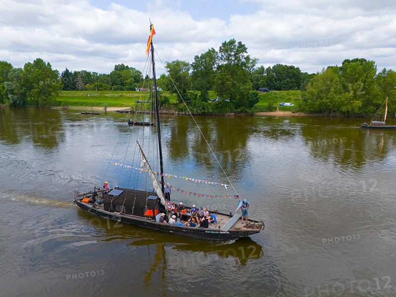 A boat sails with passengers on a calm river, surrounded by green landscape and trees under a cloudy sky, aerial view, Les Bateliers de Saint Chenonceaux, The Boatmen of Saint Chenonceaux, Loire, France, Europe