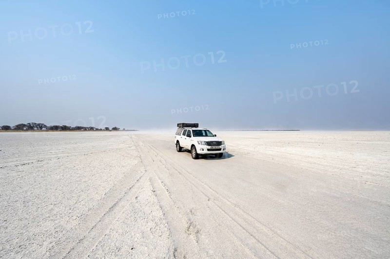 Four-wheel drive Toyota Hilux with roof tent, driving over salt pan, lone car in large wide plain, Nxai Pan National Park, Botswana, Africa