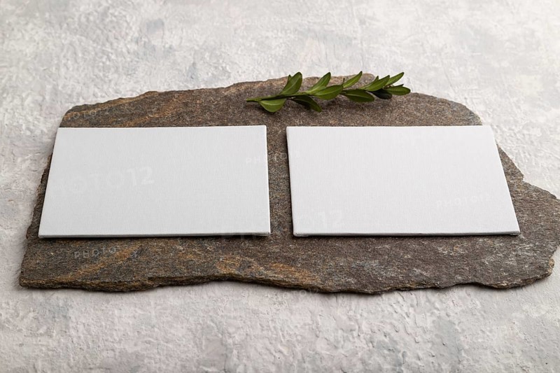 White paper business card, mockup with natural stone and boxwood branch on gray concrete background. Blank, side view, still life, canvas, copy space